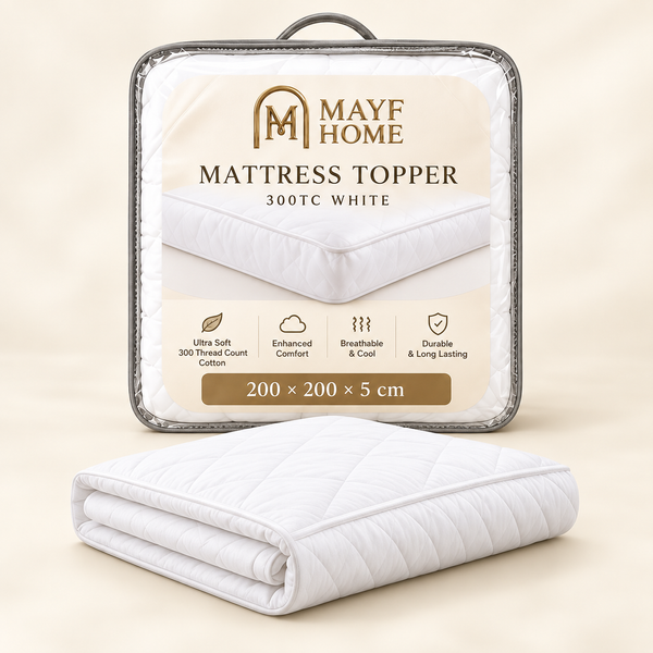 A folded white quilted mattress topper is shown in front of its retail packaging. The packaging is a clear plastic case with a printed label reading 'MAYF HOME MATTRESS TOPPER 300TC WHITE 200 x 200 x 5 cm' and feature icons.